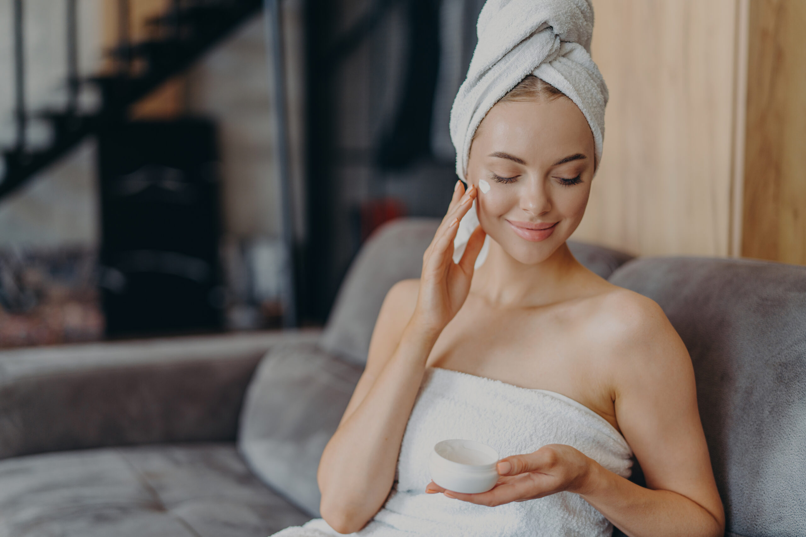 Woman applying face cream, towel wrapped around.